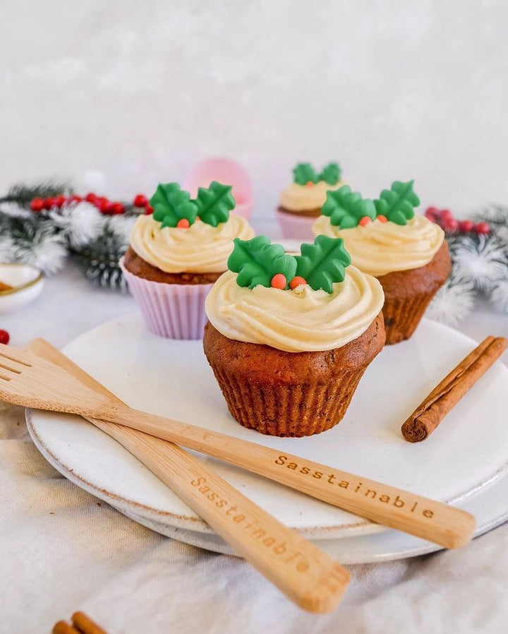 Three cupcakes topped with holly-shaped icing, on a plate with a stick of cinnamon.