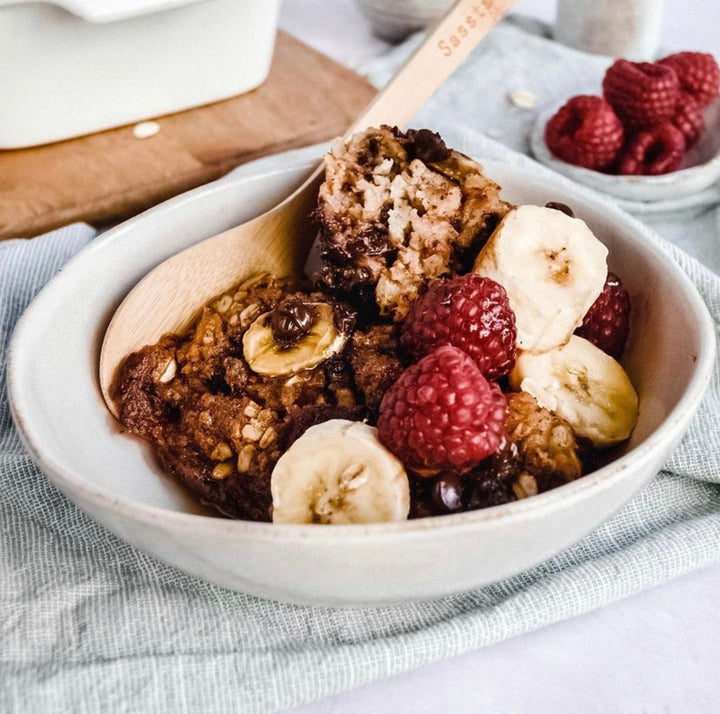 Chocolatey baked oats served in a bowl with fruit and a bamboo spoon