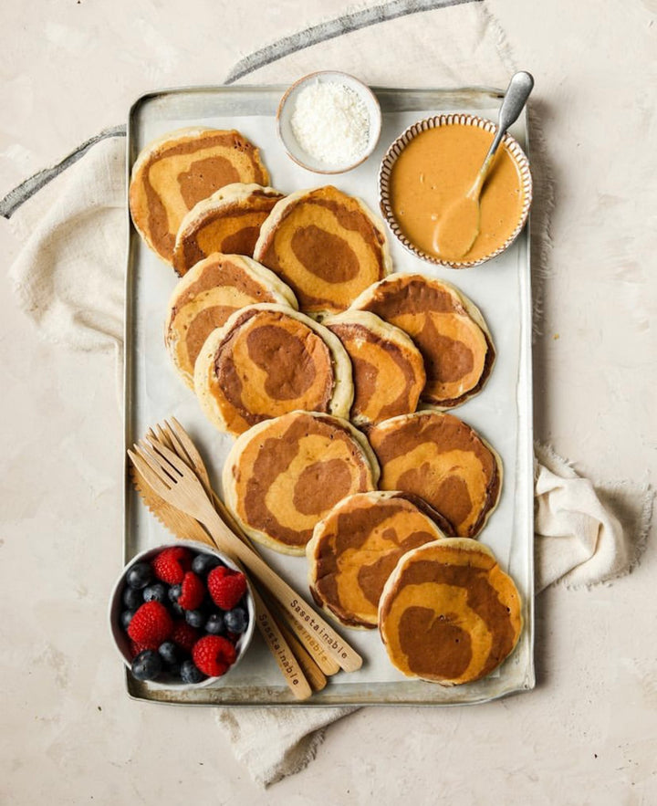 Marble-effect pancakes on a tray served with berries, coconut and peanut butter.