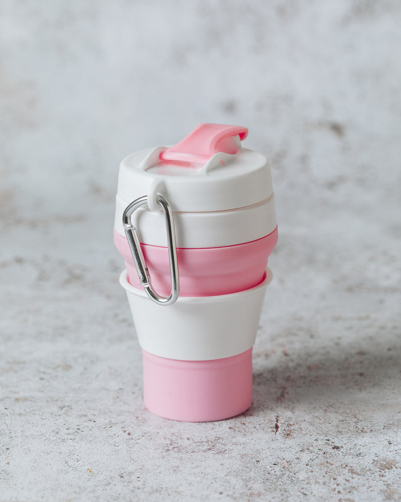 Pink and white collapsible cup expanded and sitting upright on a marble surface, with a view of the carabiner clip. 
