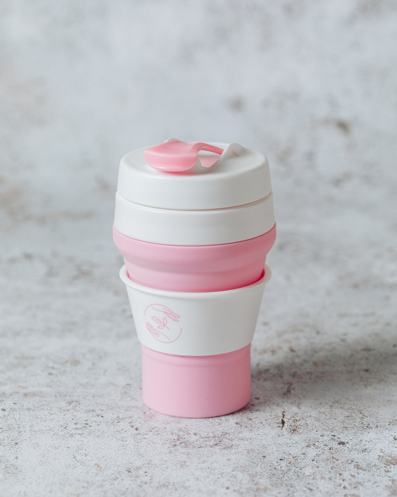 Pink and white collapsible cup expanded and sitting upright on a marble surface.