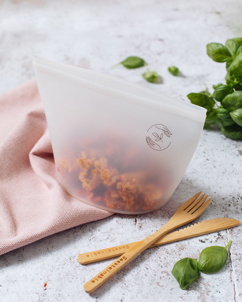 A large reusable pouch with leftovers inside, with bamboo cutlery beside it