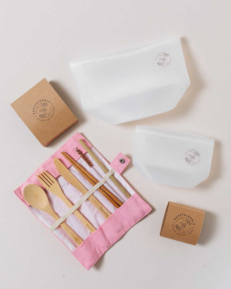 Large silicone pouch, small silicone pouch and pink cutlery set lying on a plain white background.