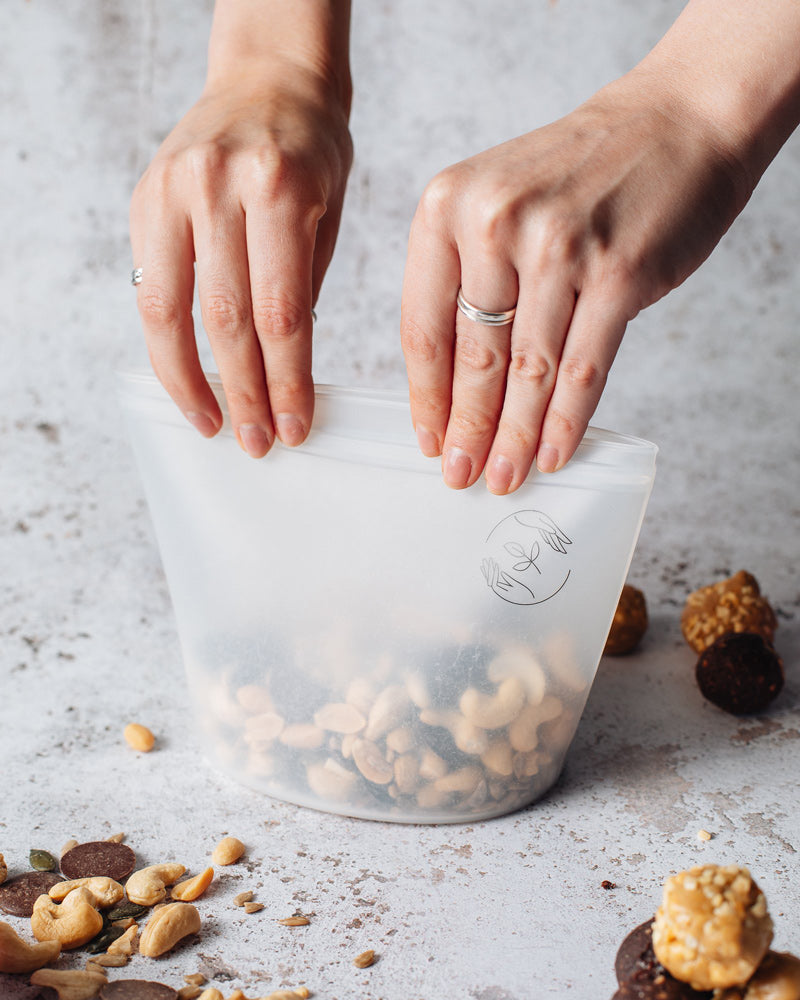 Medium silicone pouch filled with nuts being sealed by two hands.
