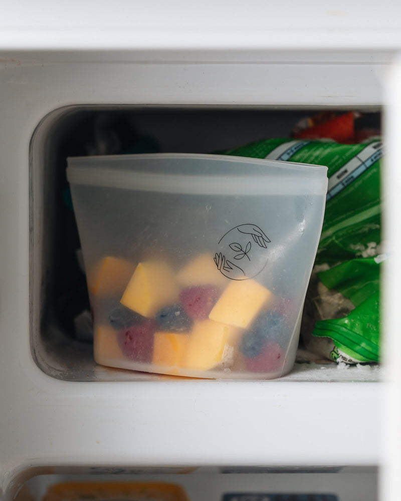 A small silicone reusable pouch containing cubed mango, raspberries and blueberries sat on an open freezer shelf.
