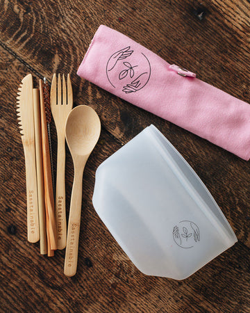 Bamboo cutlery, silicone pouch and pink canvas case with Sasstainable logo on a wooden surface.
