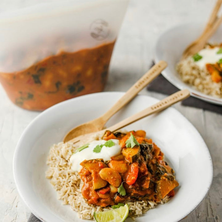 Curry and rice served on a plate with bamboo cutlery and leftovers in a pouch