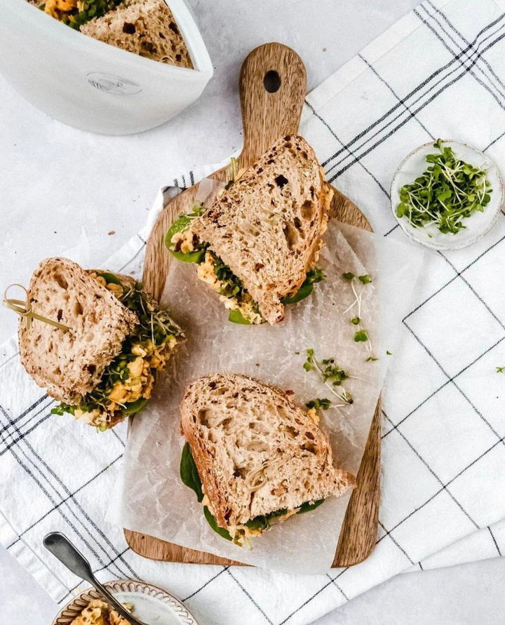 Image of a chickpea salad sandwich cut into halves on a chopping board