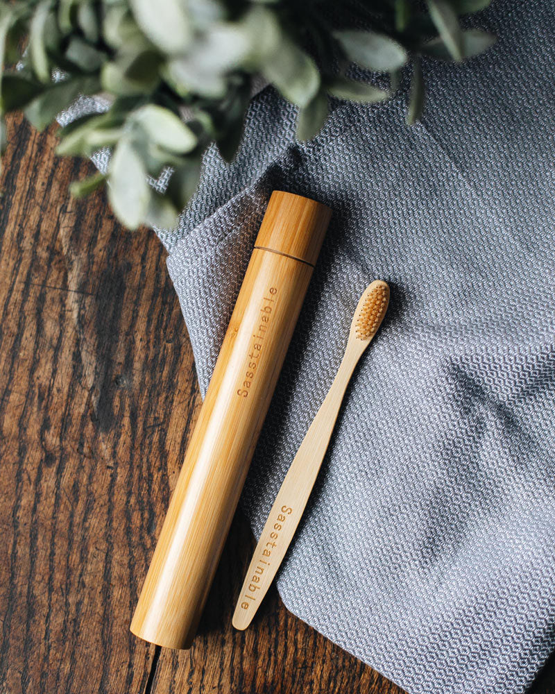 A bamboo tube and bamboo toothbrush laid flat on a blue cloth, on top of a wooden table.