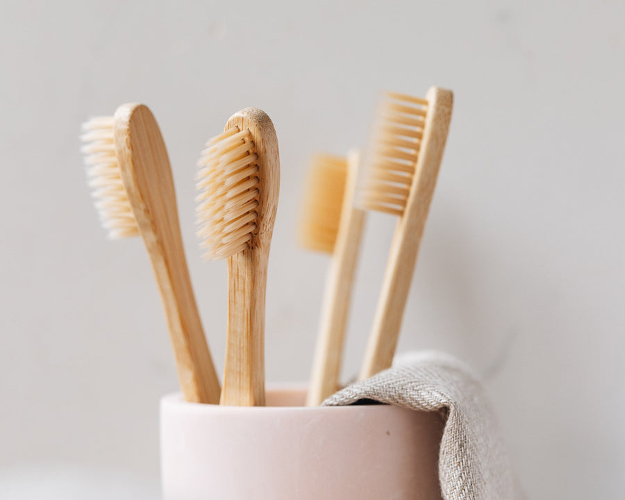 Four bamboo toothbrush heads protruding from a pink mug with a natural cloth beside it.