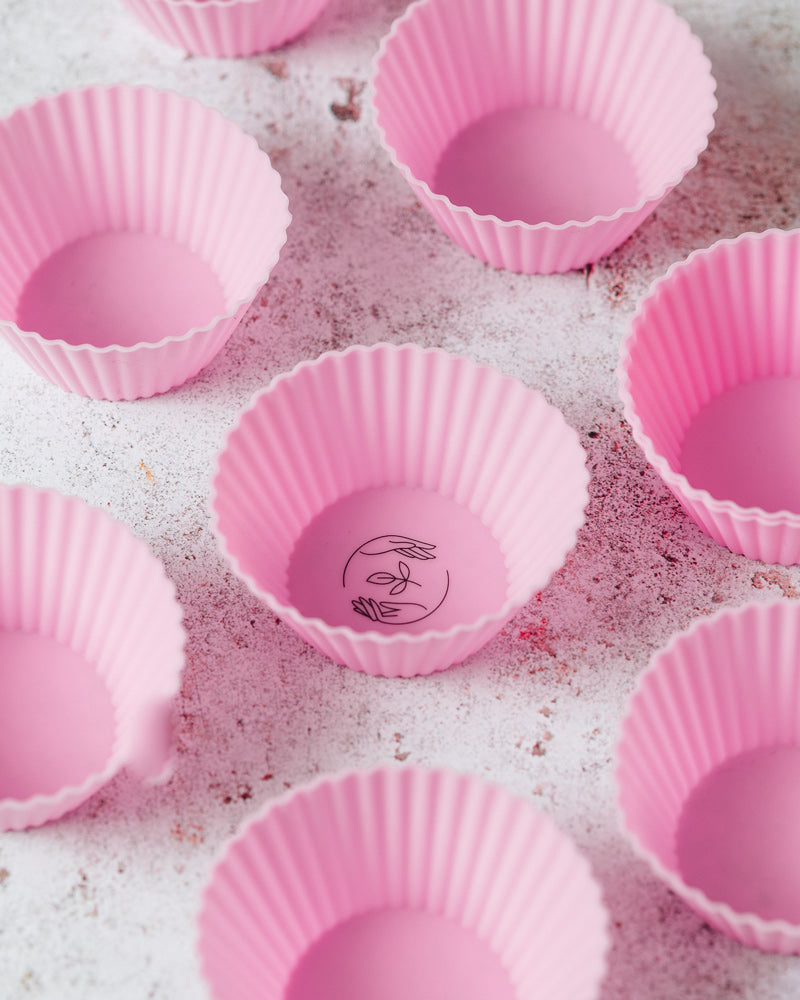 Pink reusable silicone cupcake cases featuring the black Sasstainable logo, laid out evenly across a marbled surface.