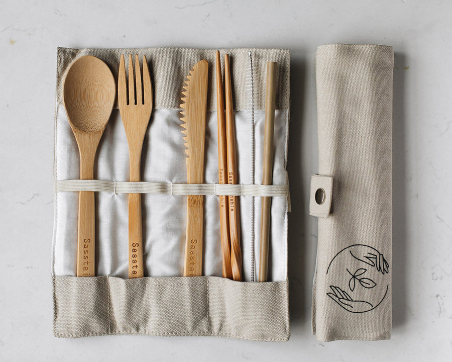 Bamboo spoon, fork, knife, chopsticks, straw cleaner and straw in a natural canvas case, next to a rolled up canvas vase, on a white background.