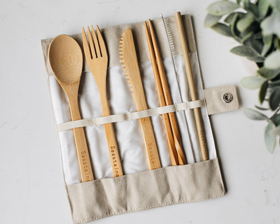 Bamboo spoon, fork, knife, chopsticks, straw cleaner and straw in a natural canvas case, on a white marble background.