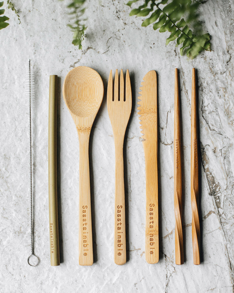 Straw cleaner, bamboo straw, spoon, fork, knife and chopsticks on a white marble background.