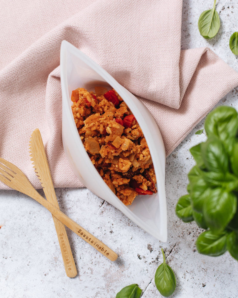 Aerial view of the large pouch containing a red rice dish, on top of a pink cloth, with a bamboo knife and fork beside it.