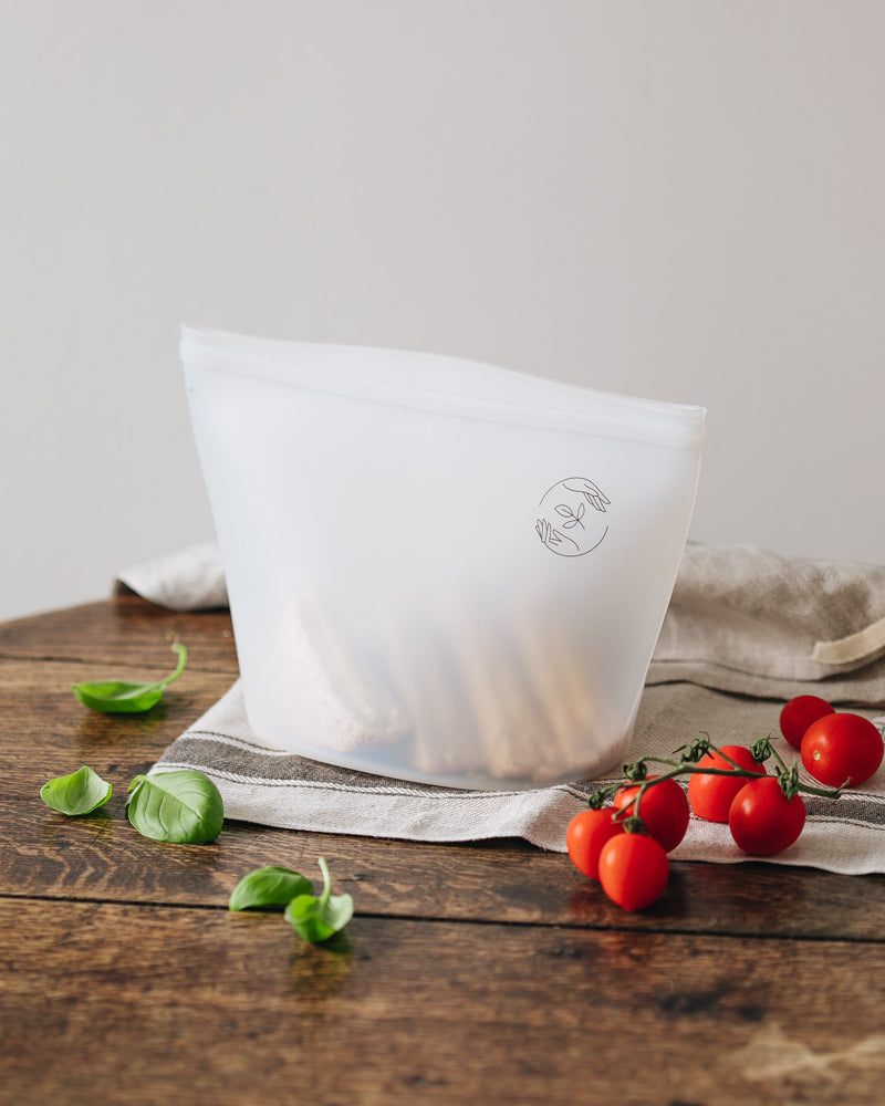 Large silicone pouch containing a sandwich on a cloth topping a wooden table with tomatoes in the foreground