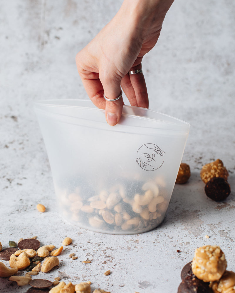 Medium silicone pouch filled with nuts being sealed by a hand.