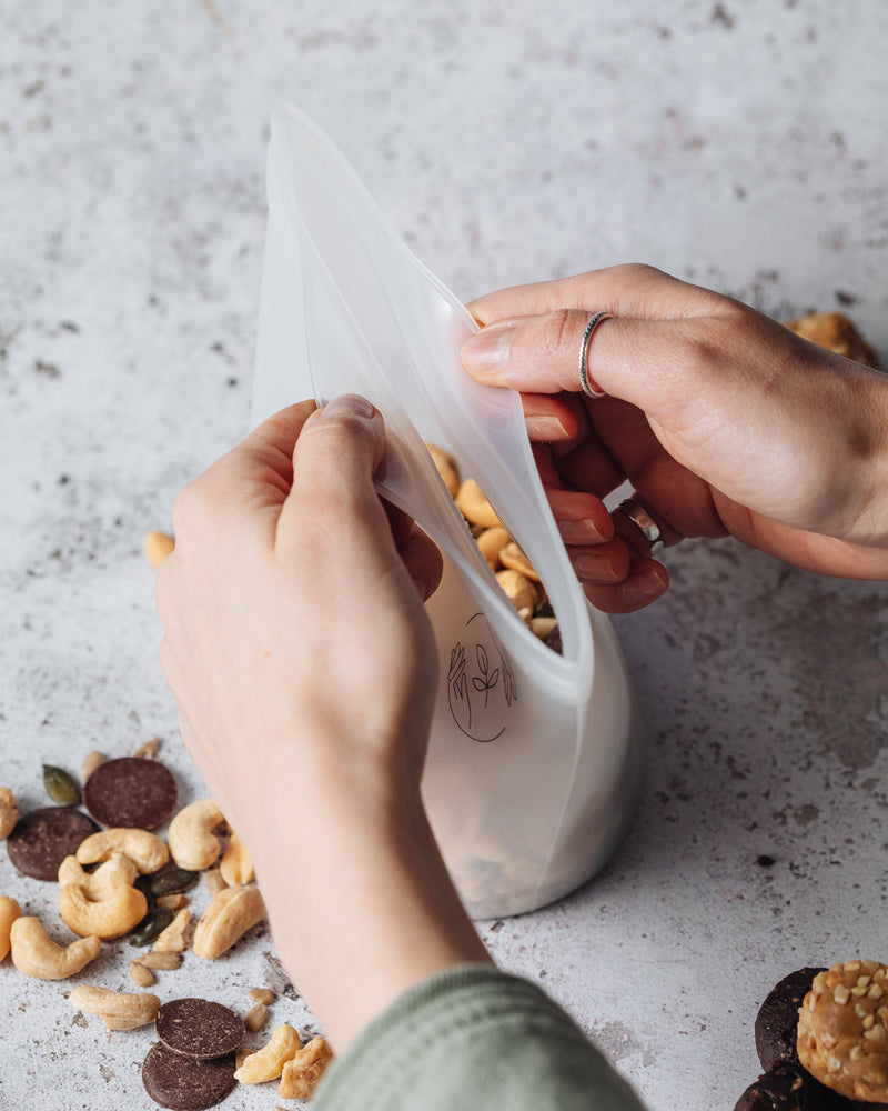 Medium silicone pouch filled with nuts being opened by two hands.