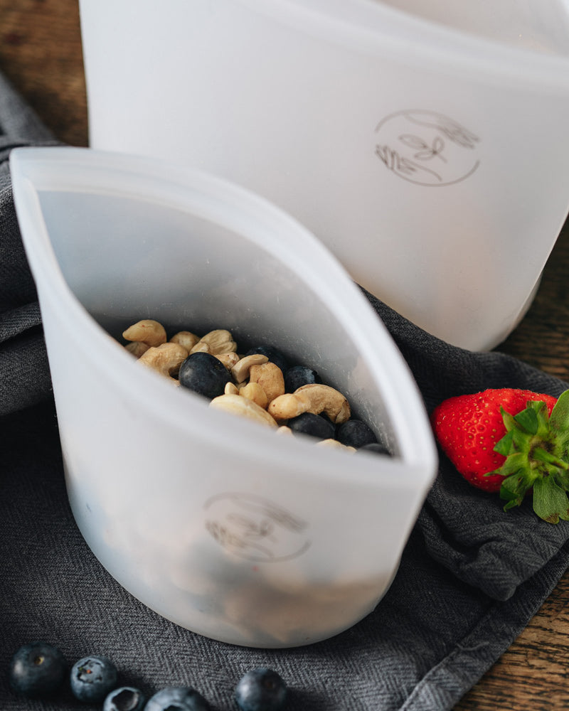 Small silicone pouch filled with nuts with large silicone pouch in the background on a dark cloth with berries strewn about.