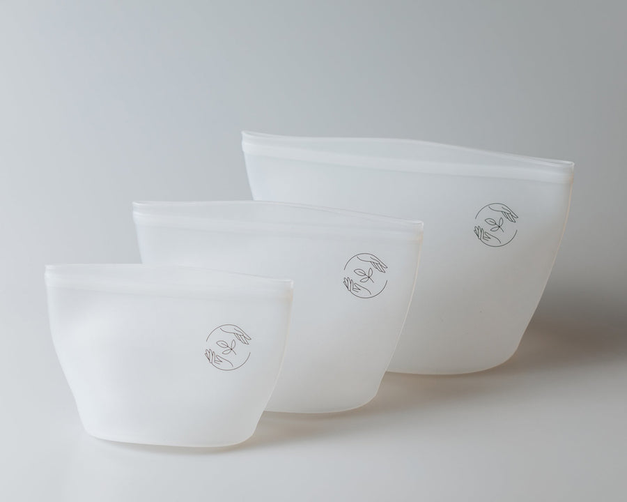 Small, medium and large reusable silicone pouches arranged from smallest in the foreground and largest in the background, on a plain white surface.