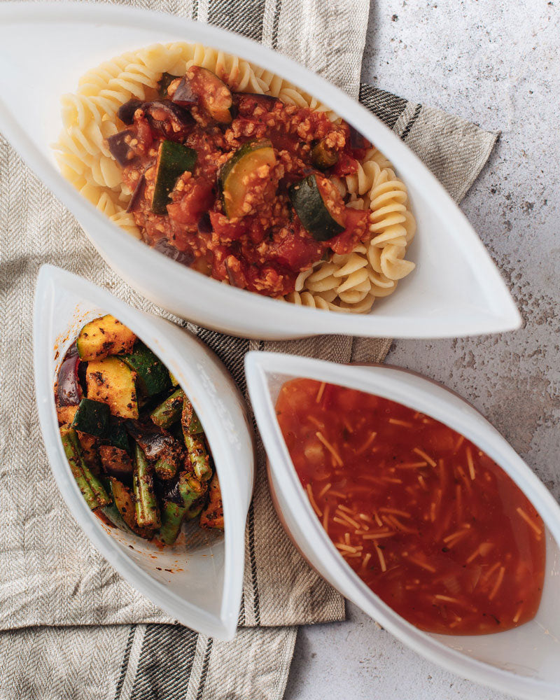 Aerial shot of a small, medium and large silicone pouch containing cooked vegetables, pasta and noodle soup.