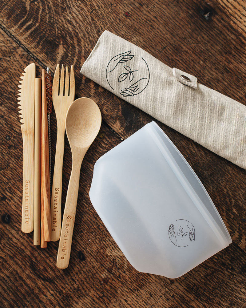 Bamboo cutlery, silicone pouch and natural canvas case with Sasstainable logo on a wooden surface.