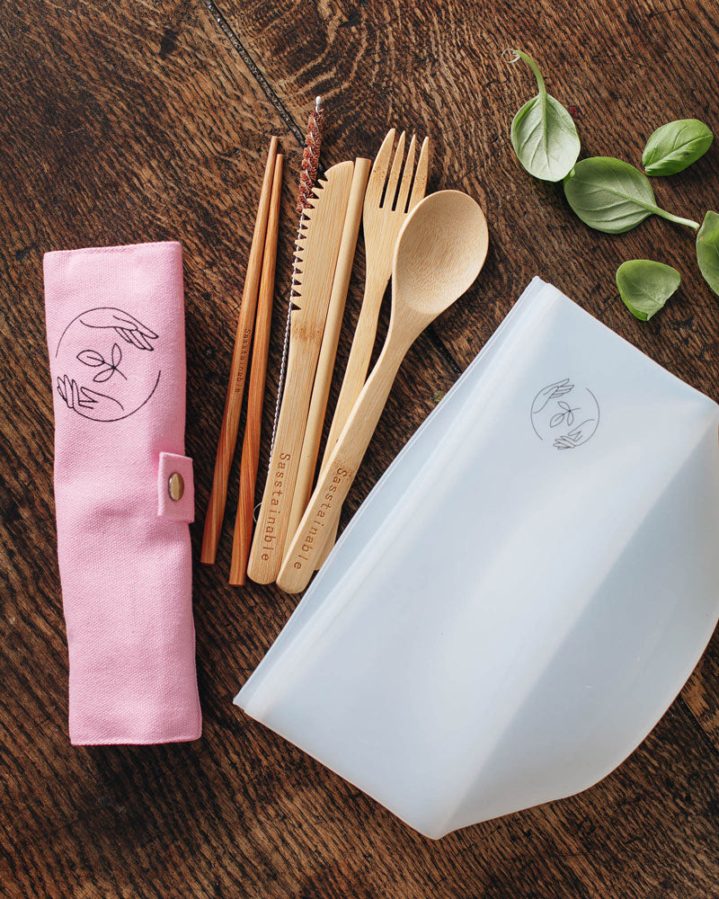 Bamboo cutlery, silicone pouch and pink canvas case with Sasstainable logo on a wooden surface.